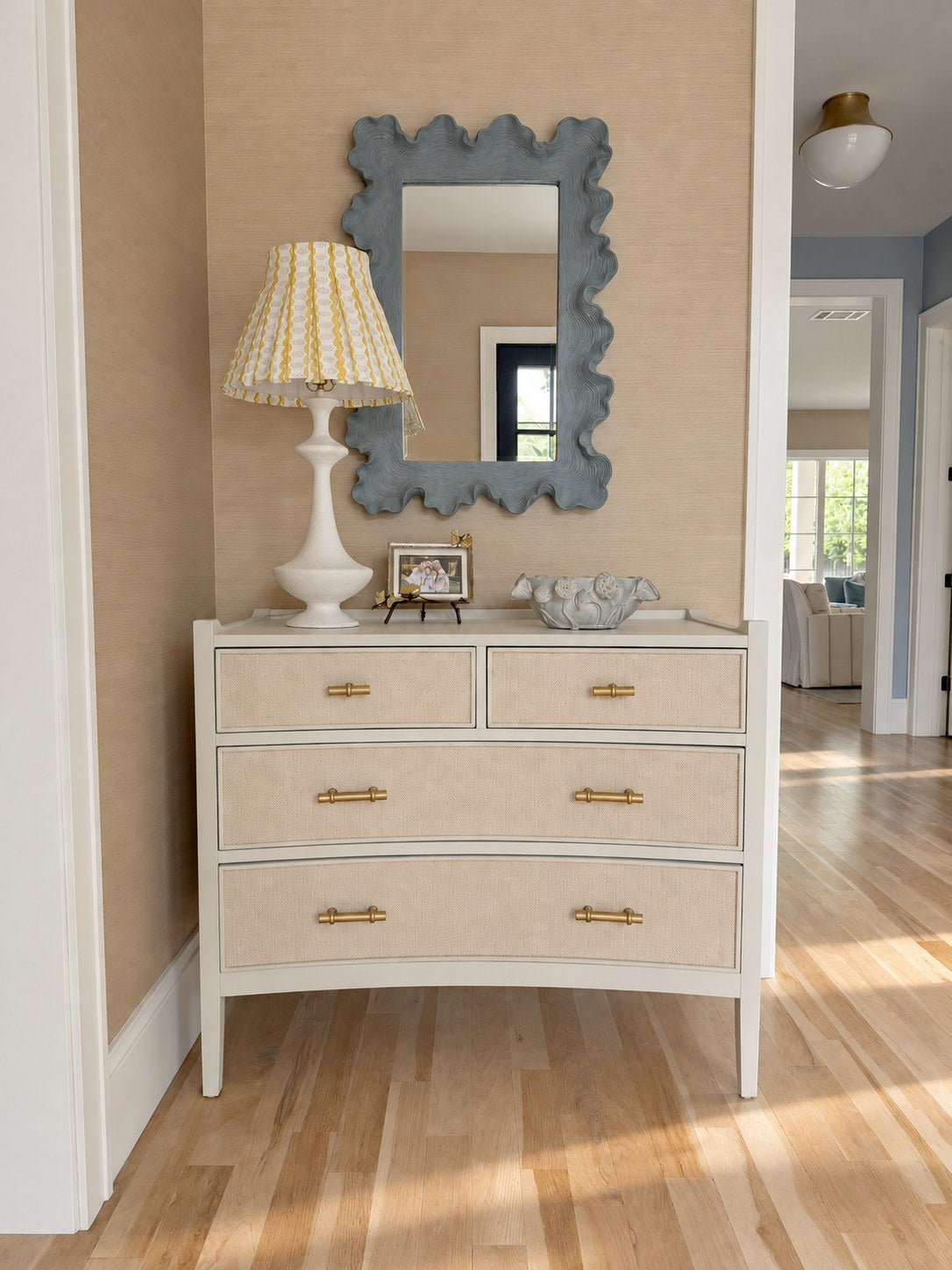 Entry with grasscloth walls, a sculpted blue mirror and raffia chest, designed by Emily Hoopes
